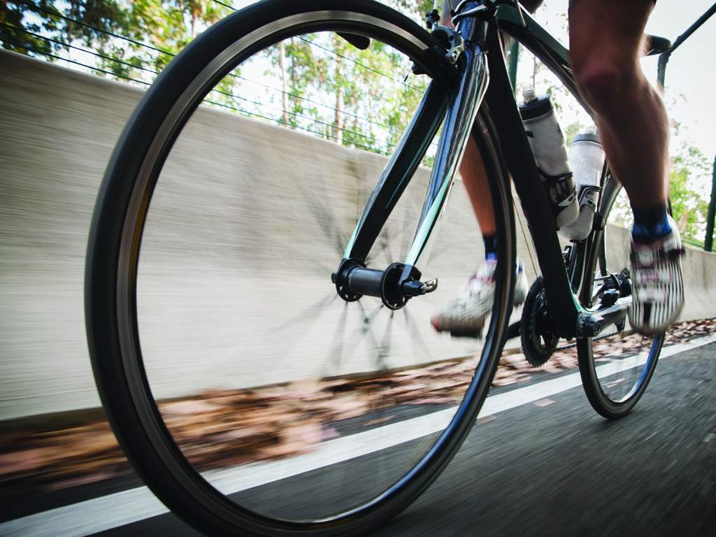 Detail of a road bike with a cyclist pedaling on a road. Photo is taken in low angle composition.