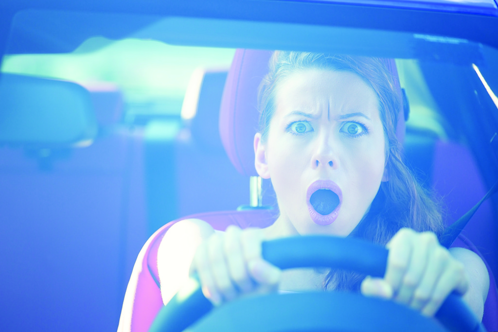 Dear in headlights. Fright face woman driving car, wide open mouth eyes, strongly squeezing wheel, front window view. Negative human face expressions, emotions, reaction. Road trip risk danger concept