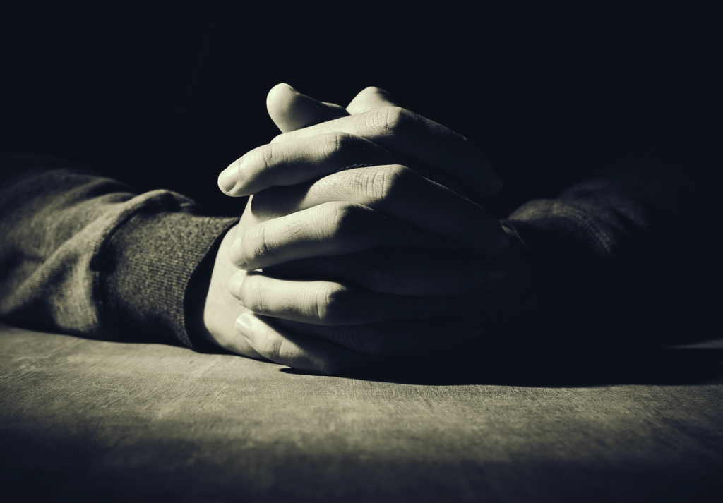 Praying hands of young man on a wooden desk background.