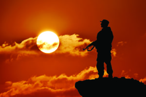 Silhouette of military soldier or officer with weapons at sunset. shot, holding gun, colorful sky, mountain, background