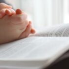 Young Child’s Hands Praying On Holy Bible
